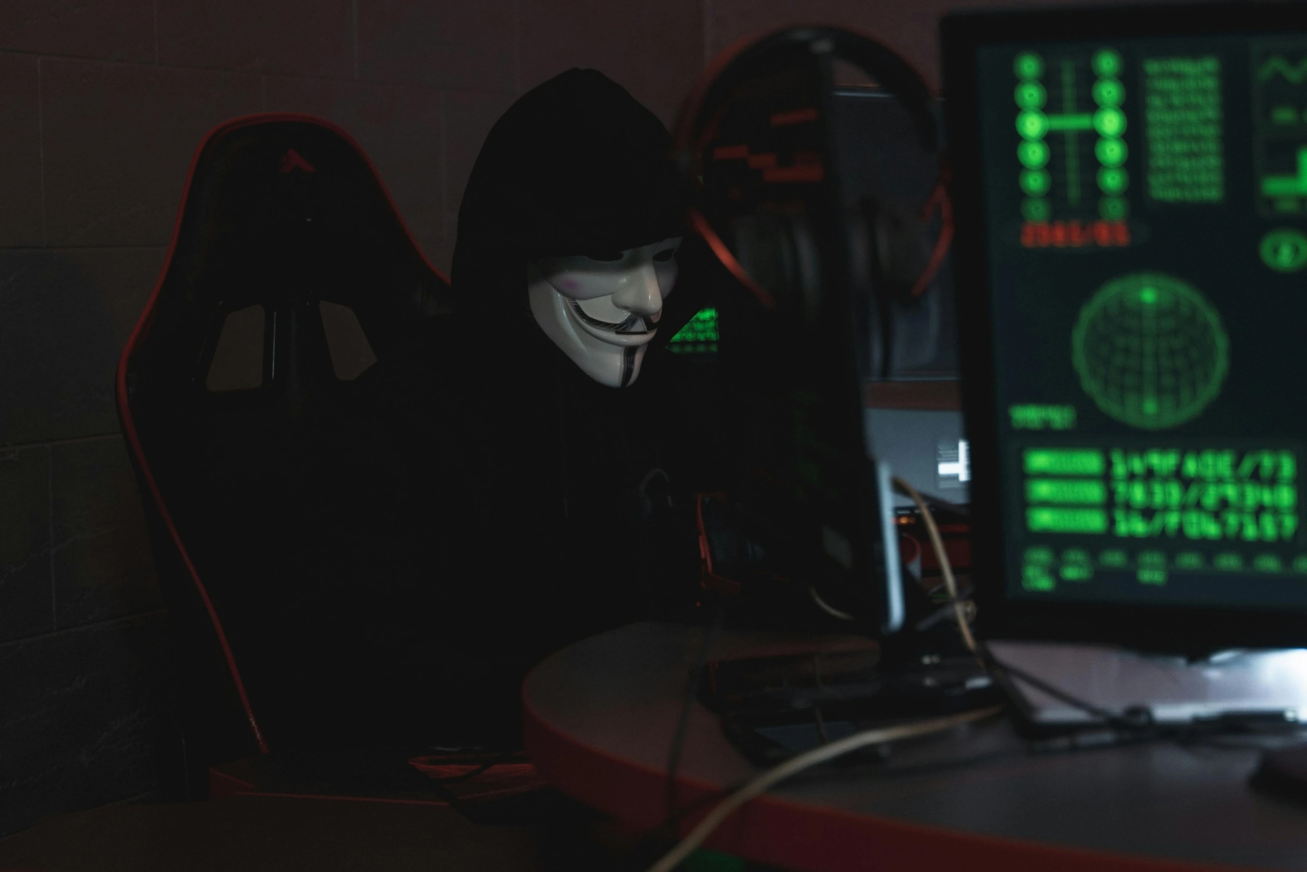 Hooded hacker at a computer with green codes in the background