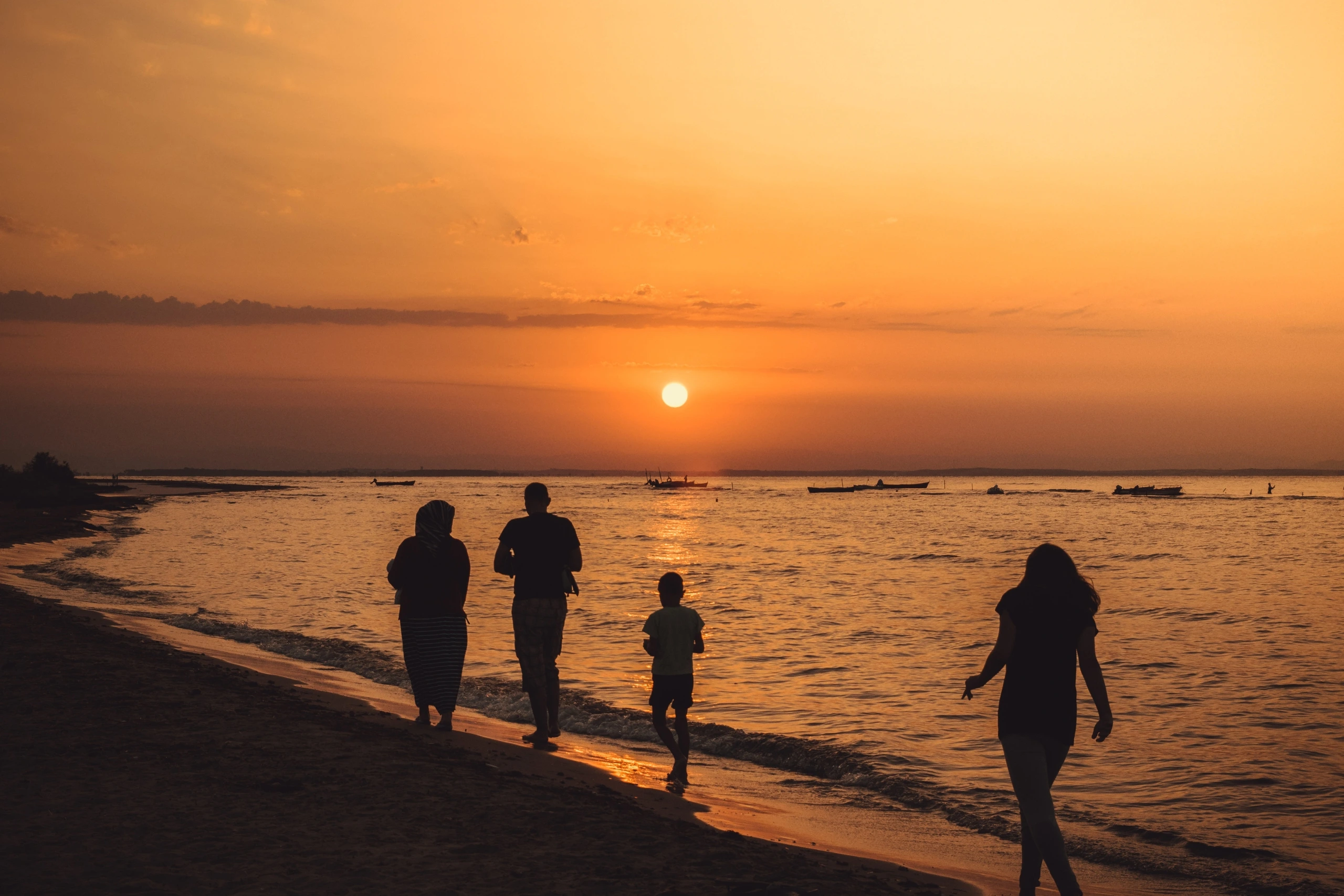 Three people walking on the beach at sunset