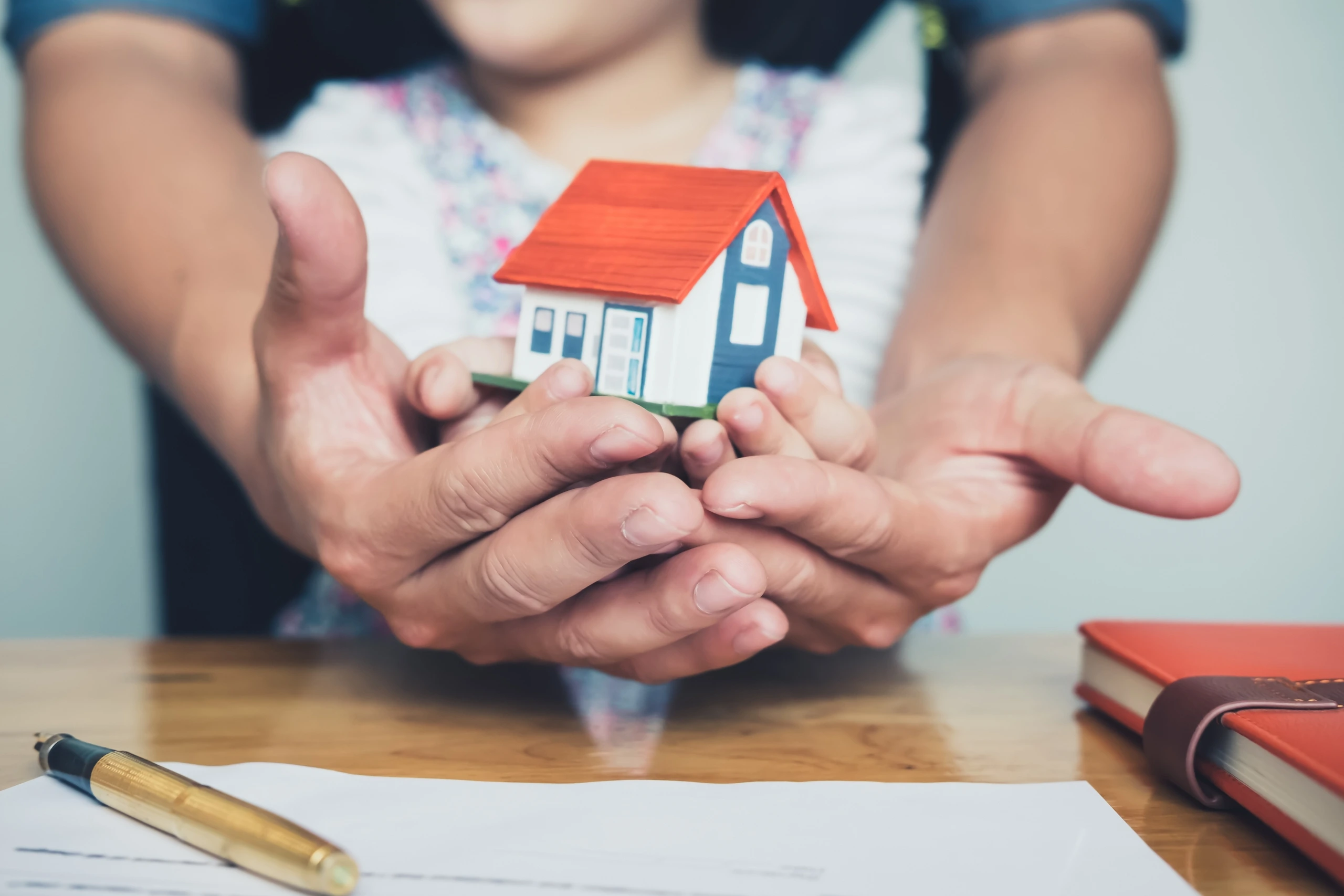 Hands holding a miniature house, symbolizing family home