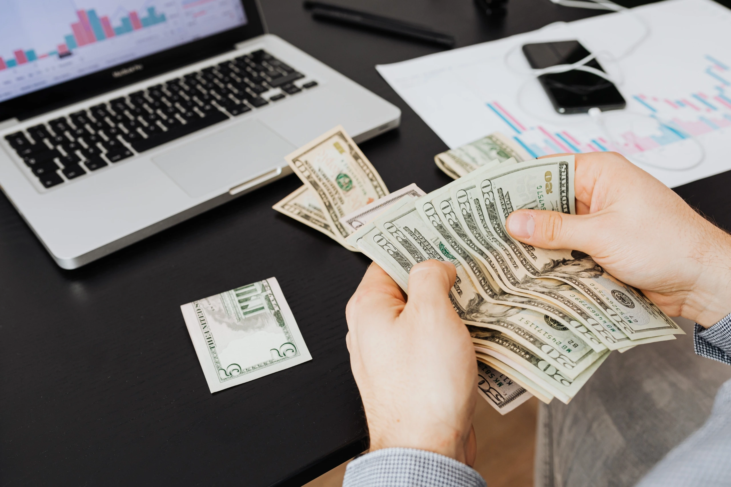 Hand counting cash on a desk next to a laptop