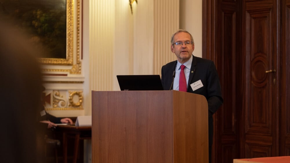 Férfi előadó beszédet tart a Central European Academy logója előtt