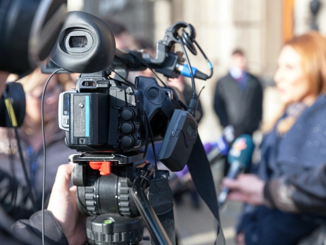 Professional camera at a press event, with journalists in the background.