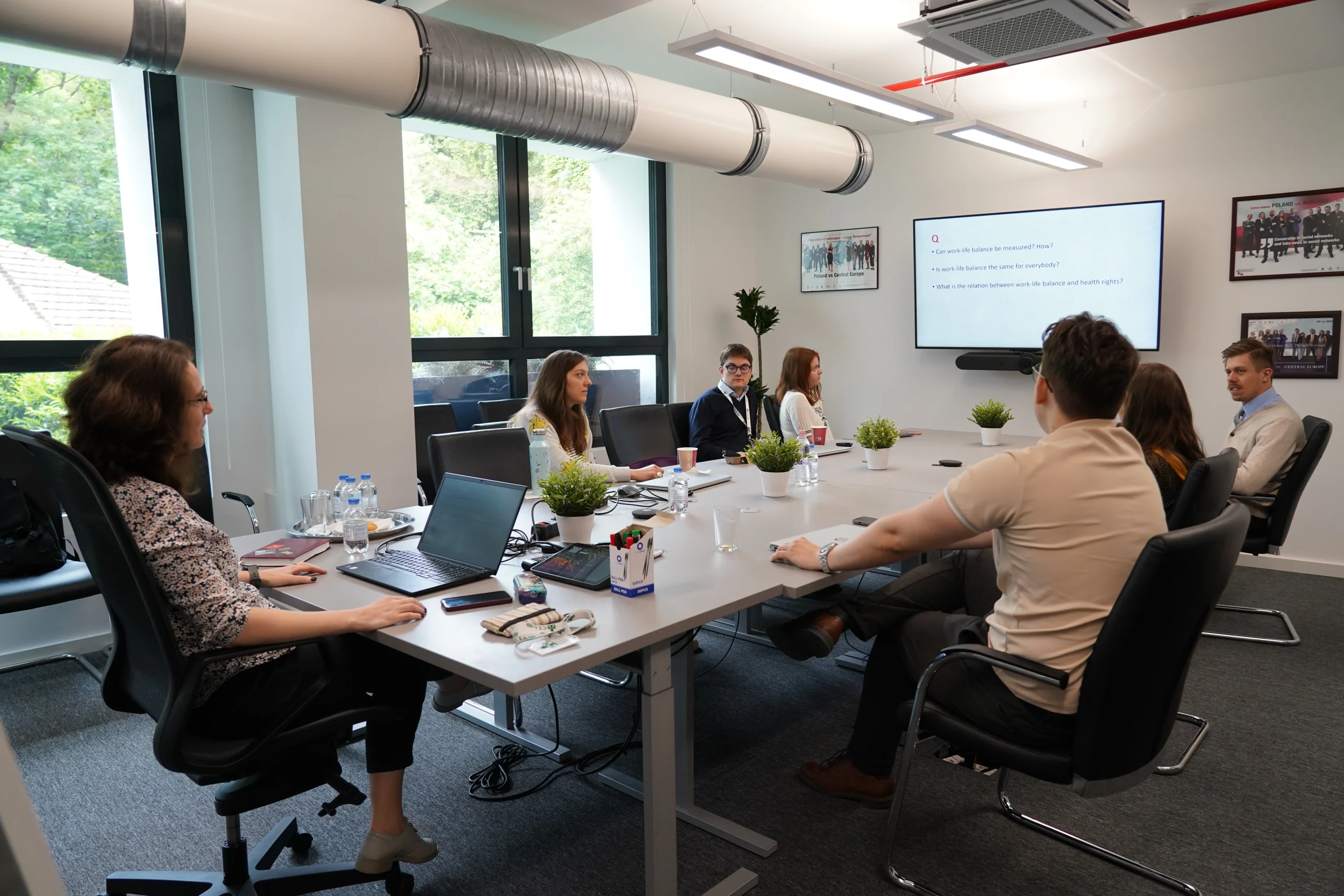 Résztvevők ülnek a tárgyalóteremben, a kivetítőn angol nyelvű kérdések láthatók.