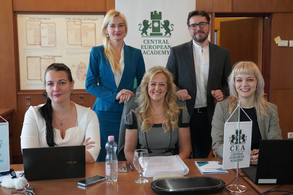 Öt fős csoport ül és áll egy tárgyalóban, a Central European Academy logója előtt.