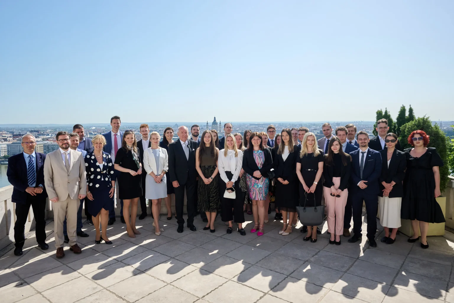 Group photo on the terrace of the Sándor Palace featuring young talents and invited guests, with the panorama of Budapest in the background.