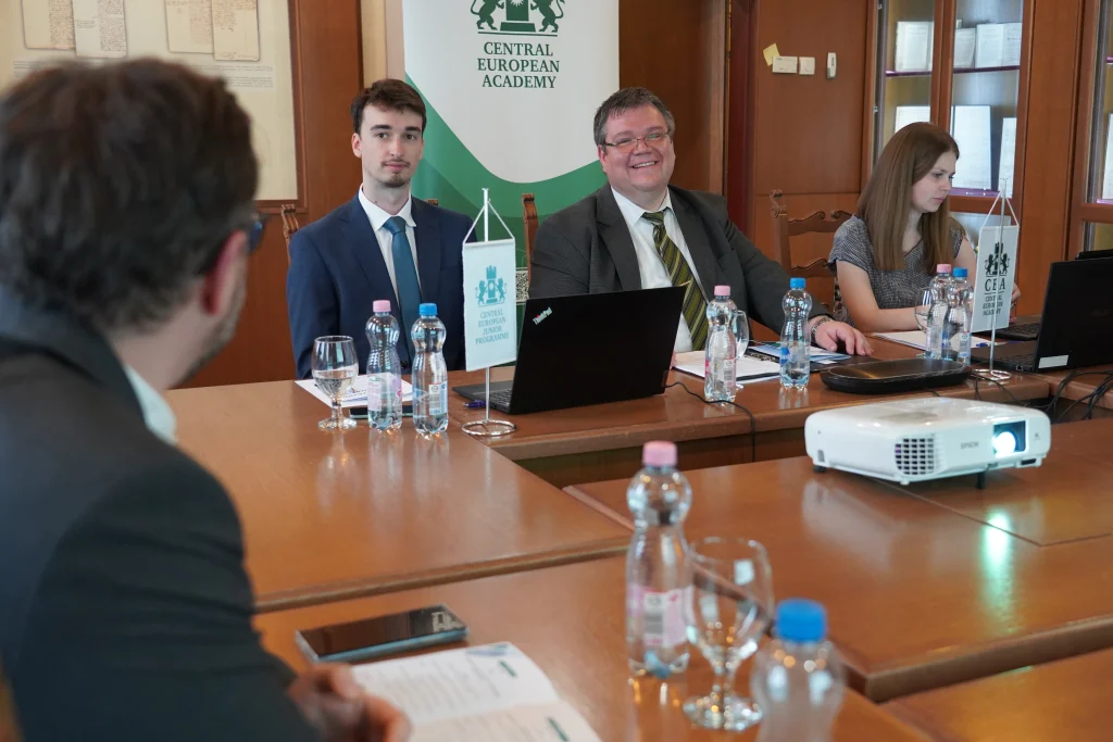 Résztvevők tárgyalóban beszélgetnek, az asztalon projektor és zászló látható.