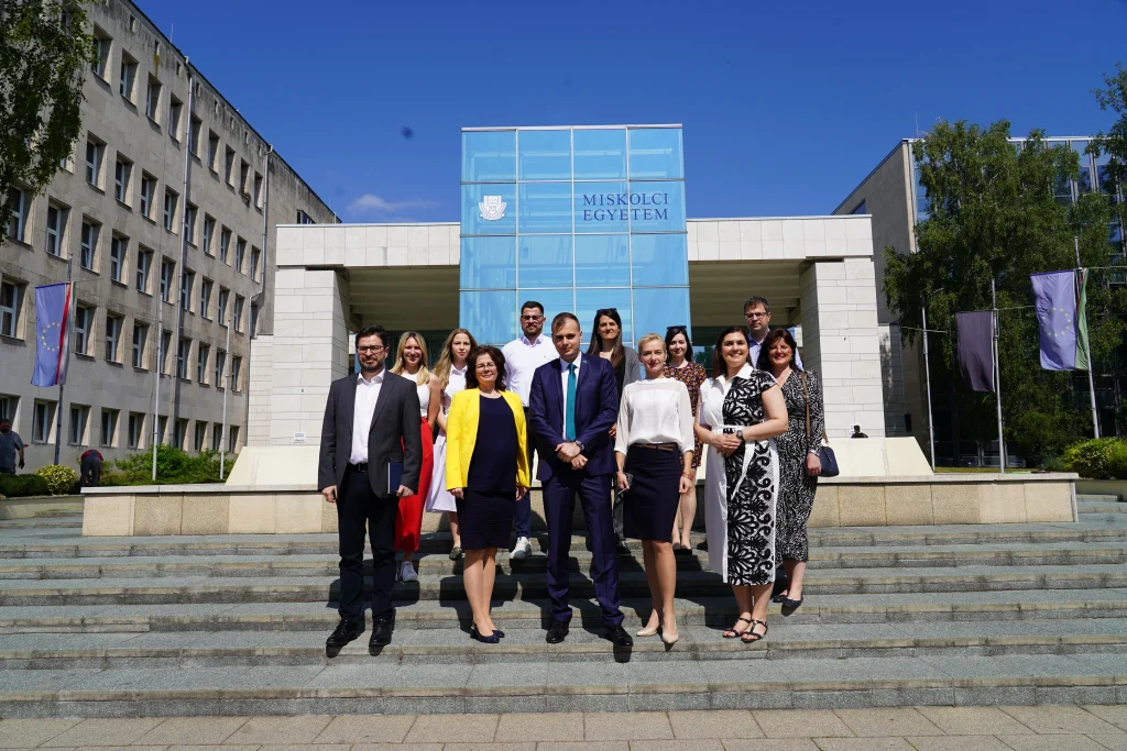 Csoportkép a Miskolci Egyetem előtt, résztvevők hivatalos és alkalmi öltözetben.