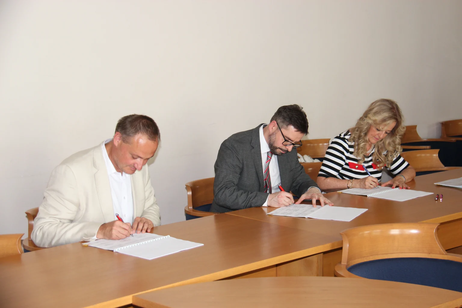 Three people ceremoniously sign a cooperation agreement at a conference table.